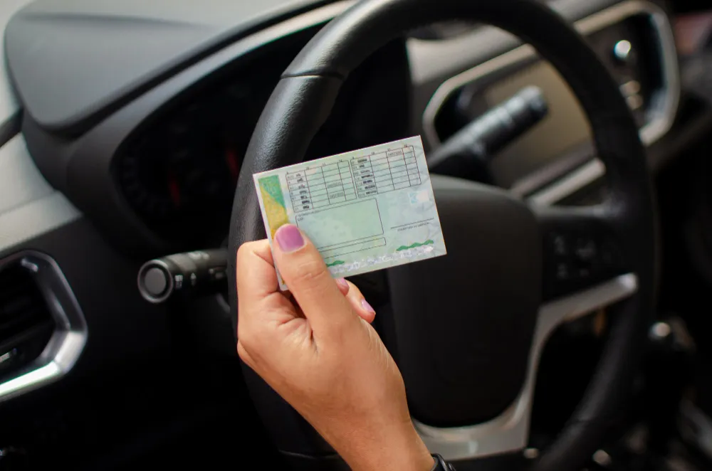 Mão segurando documento de CNH dentro de um carro, explicando o que é indicação judicial de condutor.